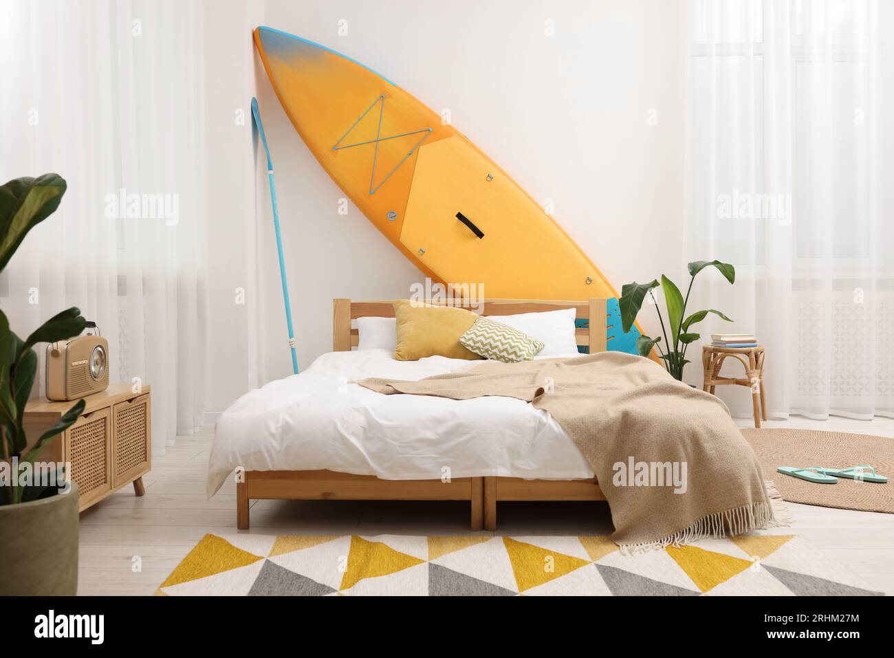 Large comfortable bed, SUP board and green houseplants in stylish ...