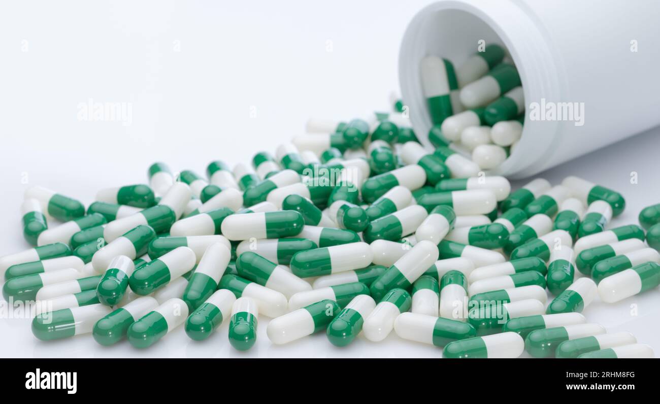 Green and white capsule pills spilled out of a white plastic bottle. Pharmaceutical industry. Prescription drug. Healthcare and medicine. Pharmacy Stock Photo