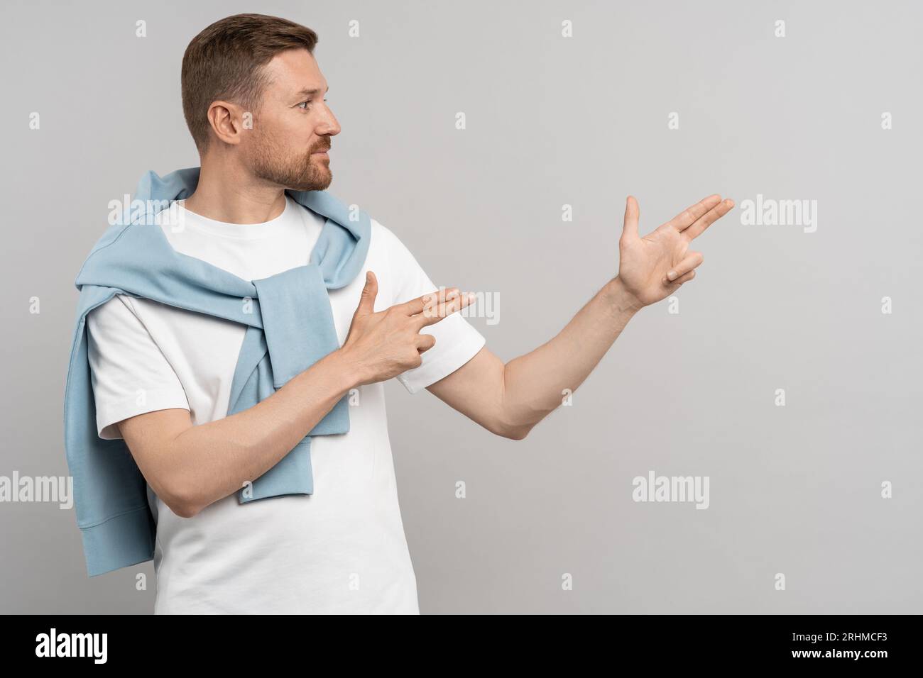 Positive young caucasian man looking and pointing fingers aside, gesturing at copy space. Stock Photo