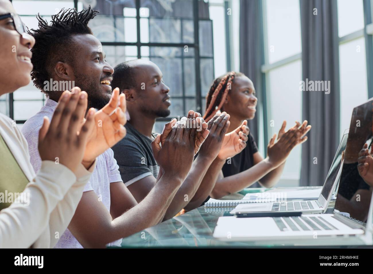Multi ethnic business group greets somebody with clapping and smiling Stock Photo