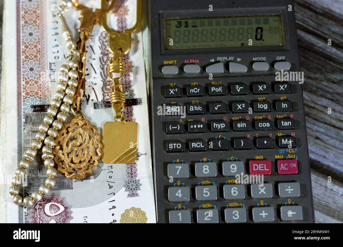 A calculator, silver rosary and gold keyring medals with a text Allahu Akbar, translation (God is the greatest), on pile of Egyptian 50 LE EGP pounds, Stock Photo