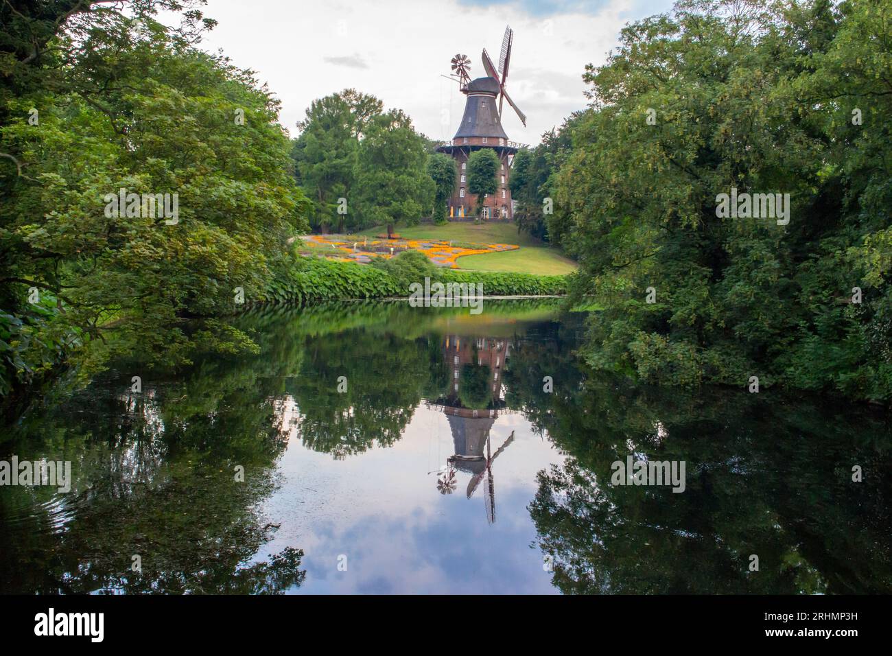 Am Wall Windmill in summer park with pond. Windmill with reflection in water in city garden. Historic architecture in Bremen. Rural german landmark. Stock Photo