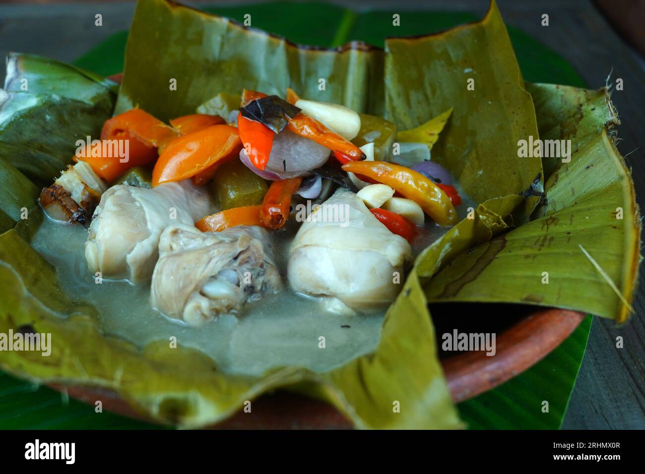 Garang Asem, the traditional Javanese food is served on a clay plate, lined with banana leaves and accompanied by a mixture of bird eye chili, tomatoe Stock Photo