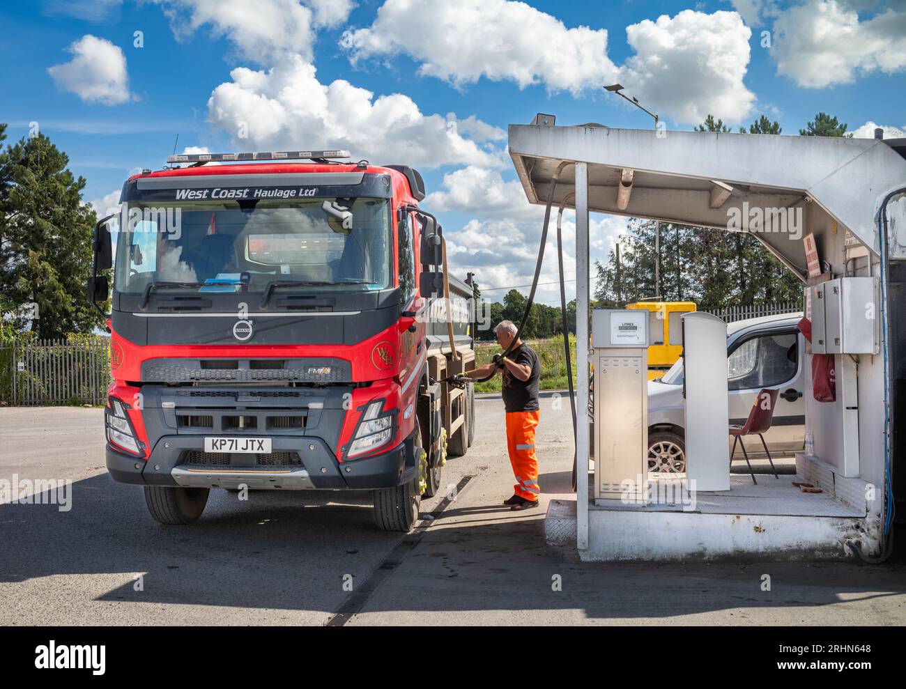 A greyhaired dump truck driver fills his red dumper truck with fuel at the Lincoln Farm Truck
