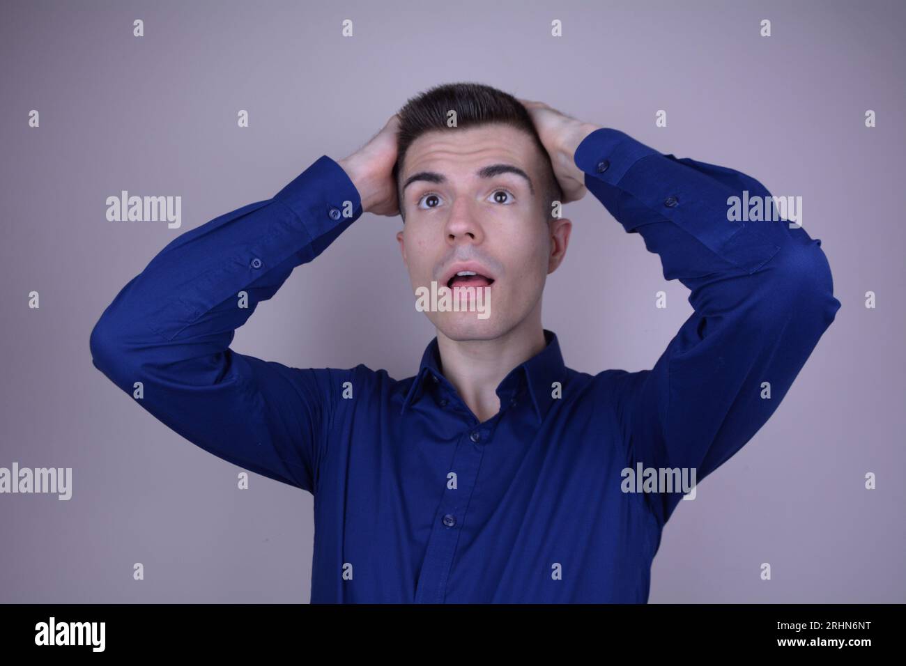 Elegant Handsome Young Man Clutches Head and Looks Up, Expression of Disbelief on Isolated Background Stock Photo
