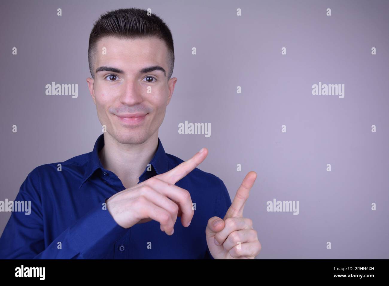 Elegant Smiling Handsome Young Caucasian Man Points Two Fingers to the Side on Isolated Background - Copy Space Stock Photo