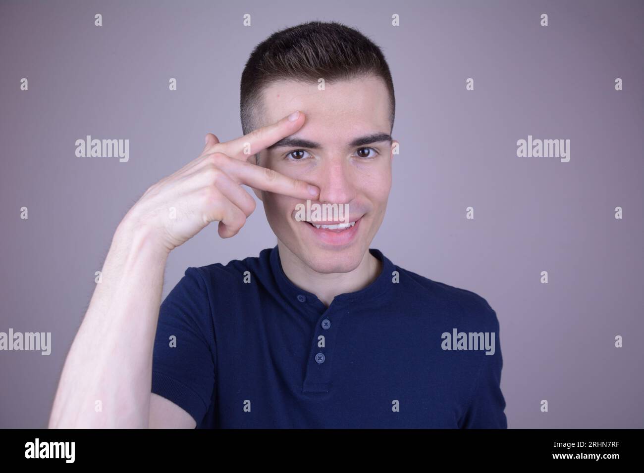 Smiling Caucasian Man with Two Fingers at Eye, Triangle Symbol on Isolated Background Stock Photo