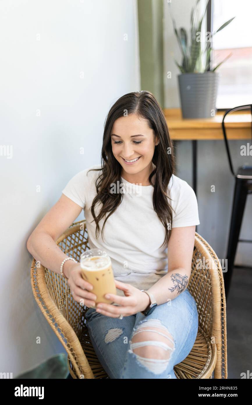 A woman sitting in a wicker chair drinking an iced latte Stock Photo