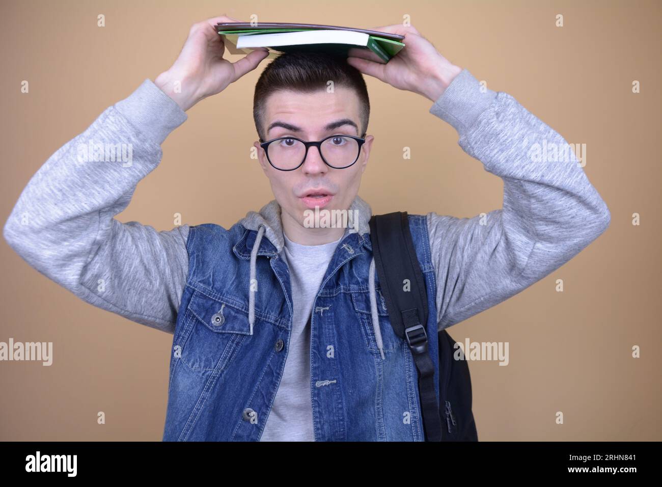 Tired Handsome Caucasian Student Balancing Textbooks and Notebooks on Head on Isolated Background Stock Photo