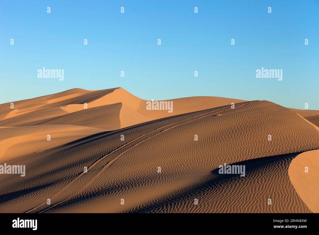 Sand dunes at sunset wheel ruts and blue sky at sunset Stock Photo