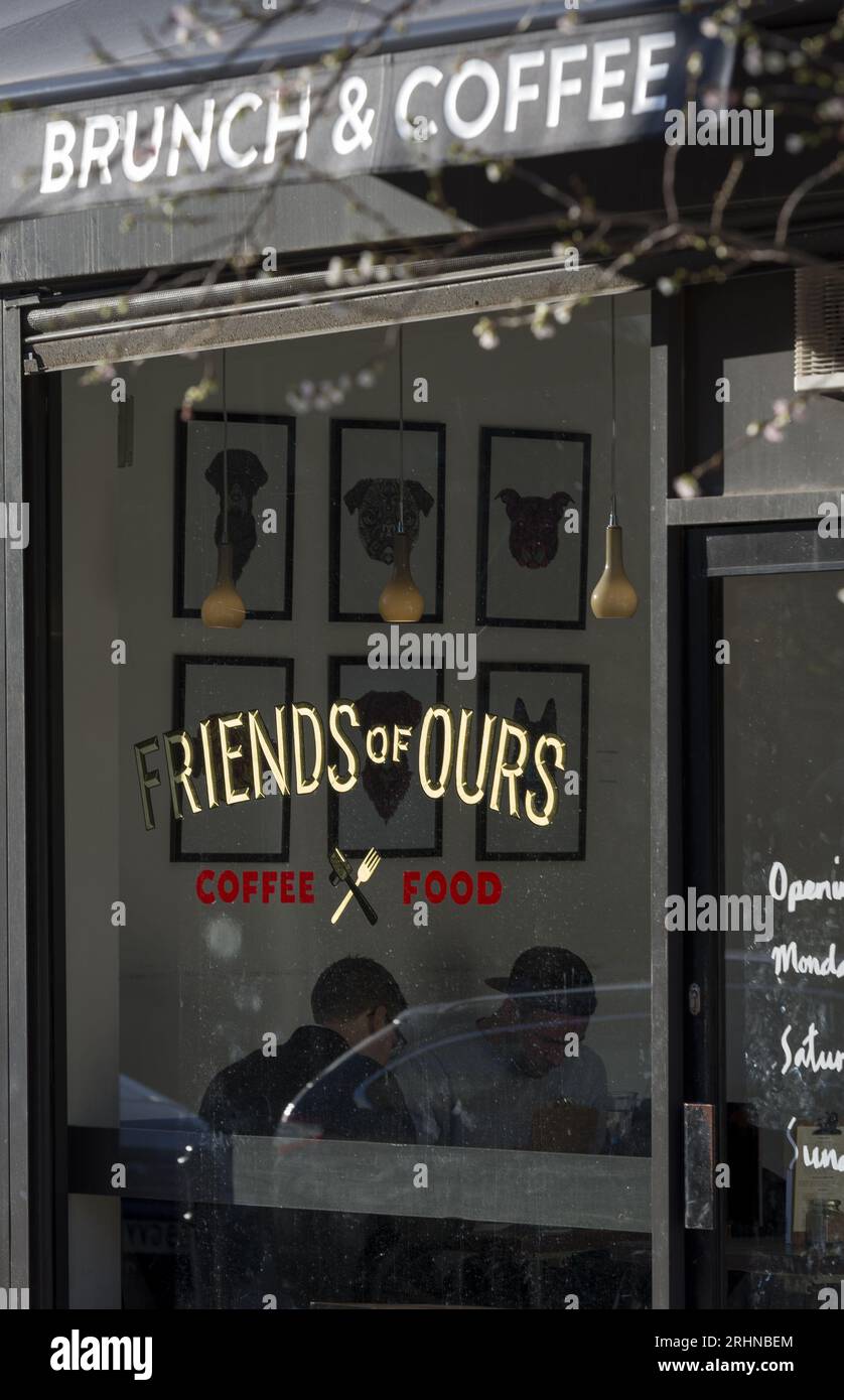Street view of Friends of Ours café in East London, with window signage, framed art, and visible diners enjoying brunch and coffee. Stock Photo