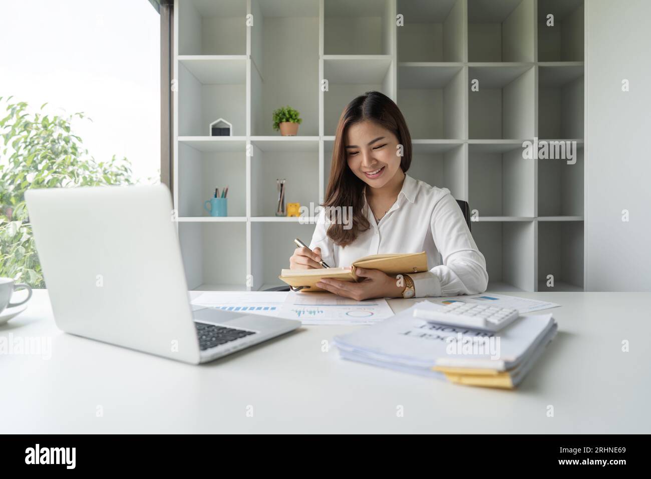 Happy and beautiful young Asian businesswoman is taking notes on her ...