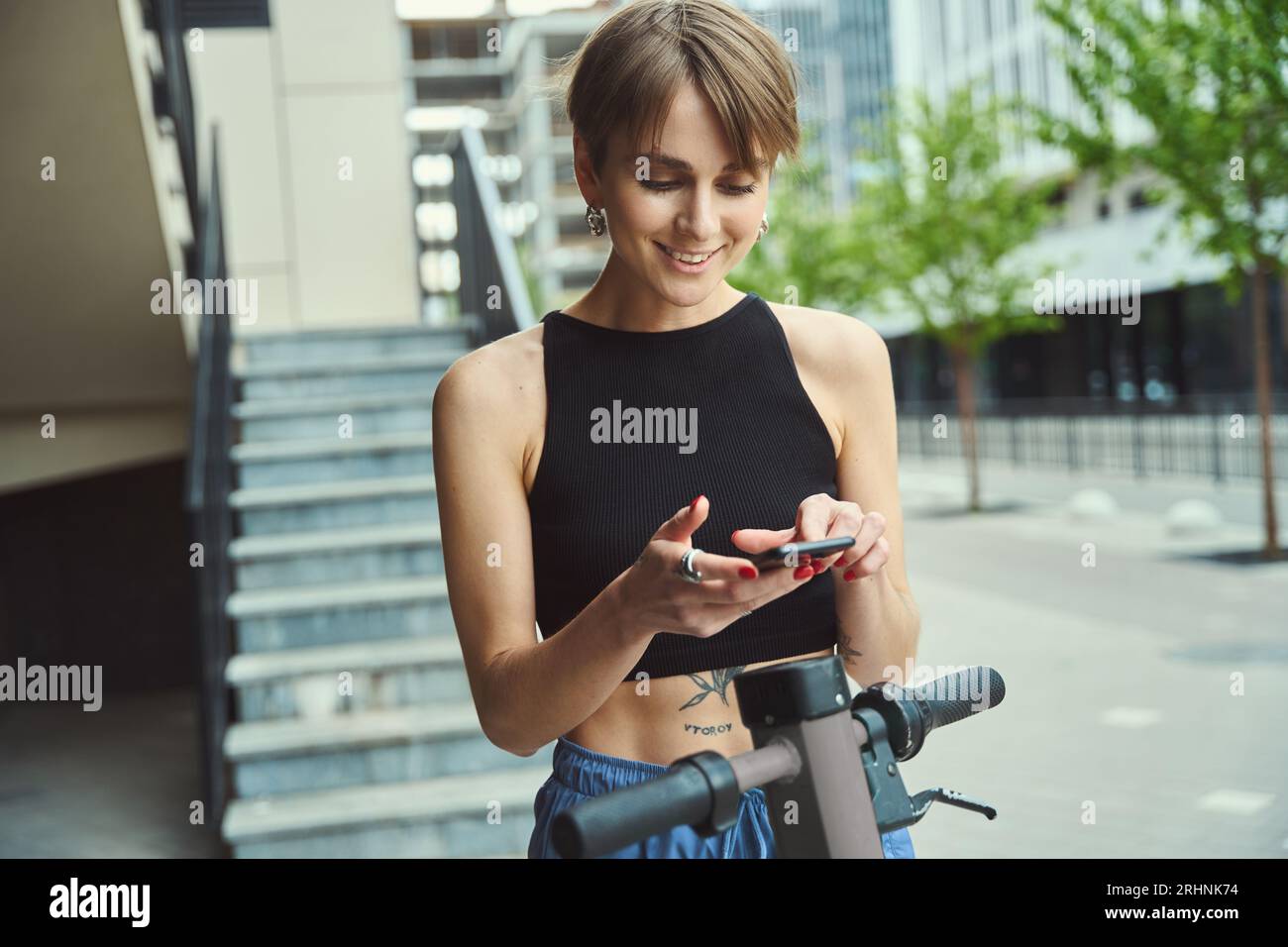 Modern young city woman stands with scooter on city street Stock Photo