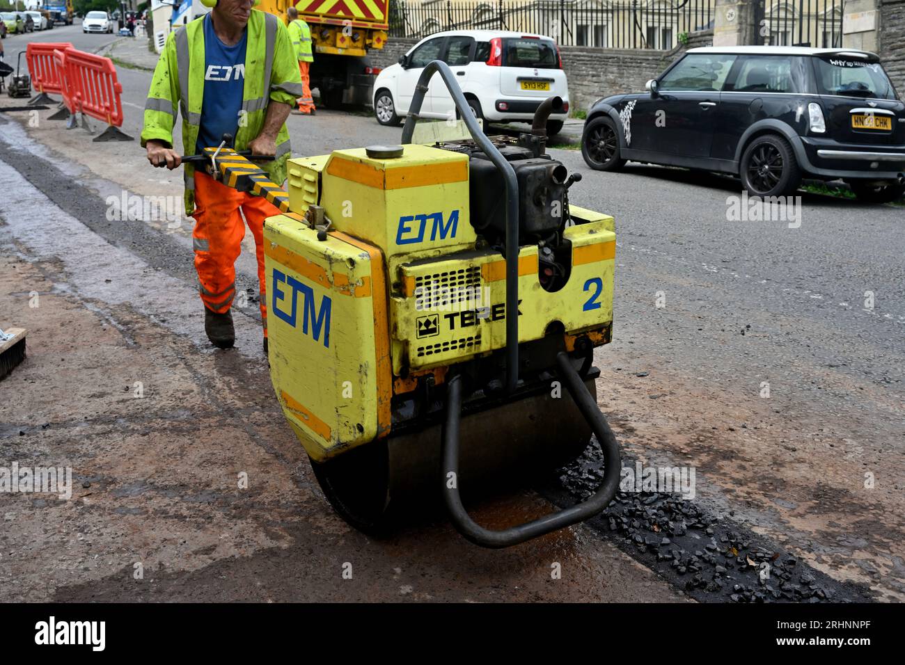 Compacting with vibrating roller finishing trench cut in road for fibre optic duct in communications upgrade, UK Stock Photo