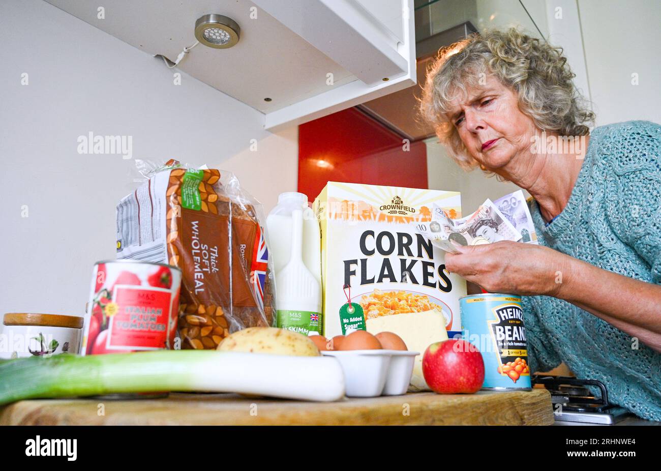 Woman at home in kitchen with variety of household food items bought in 2023 during the cost of living crisis in the UK . Food includes milk eggs cheese fruit potatoes bread leeks , tins of baked beans and tomatoes  Credit Simon Dack Stock Photo