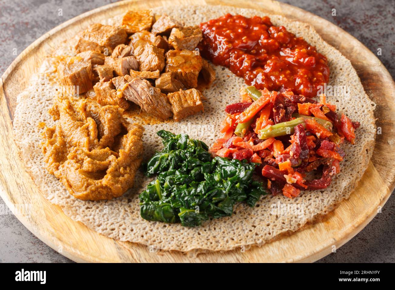 Ethiopian Injera flat bread with various vegetable and meat fillings close up on the wooden board on the table. Horizontal Stock Photo