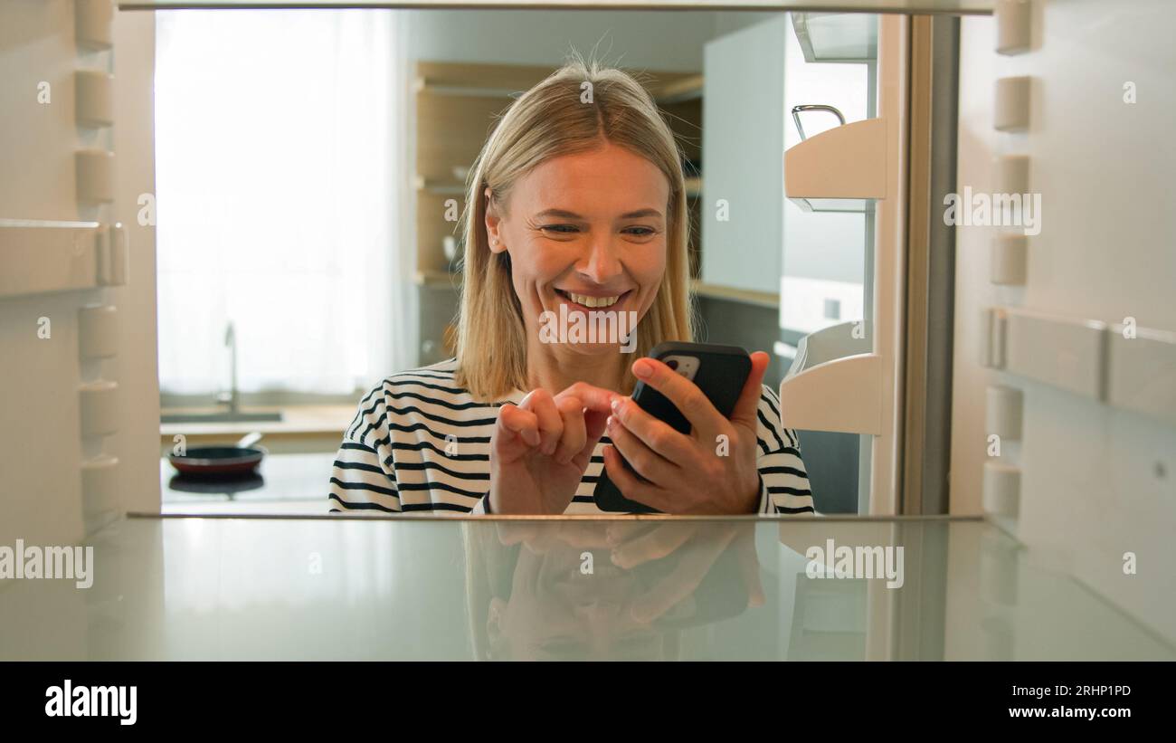 Point of view POV inside refrigerator Caucasian adult woman middle-aged female wife housewife open empty fridge order food with mobile delivery online Stock Photo