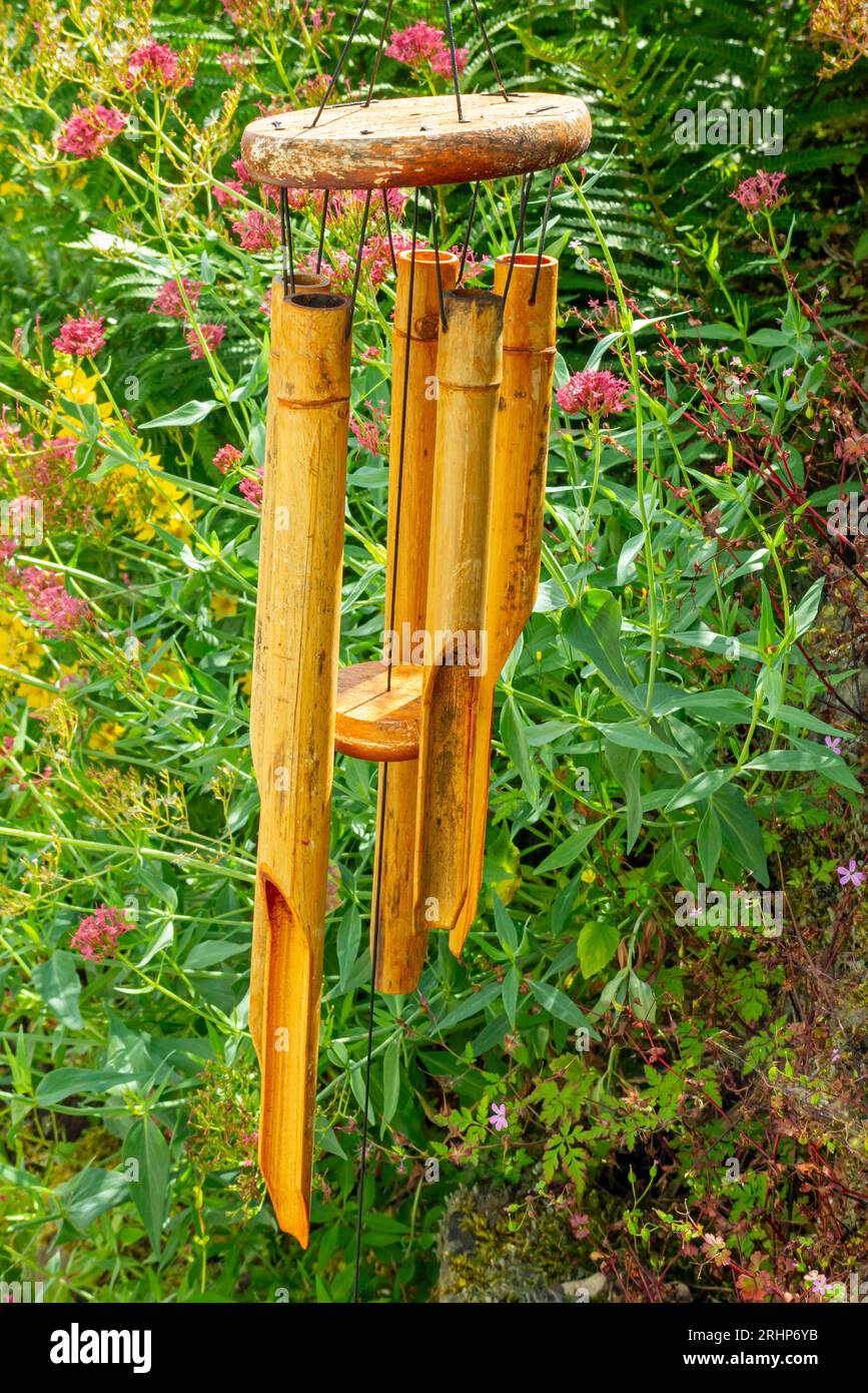 Wooden wind chimes hanging outside in a garden with flowers visible in the background. Stock Photo