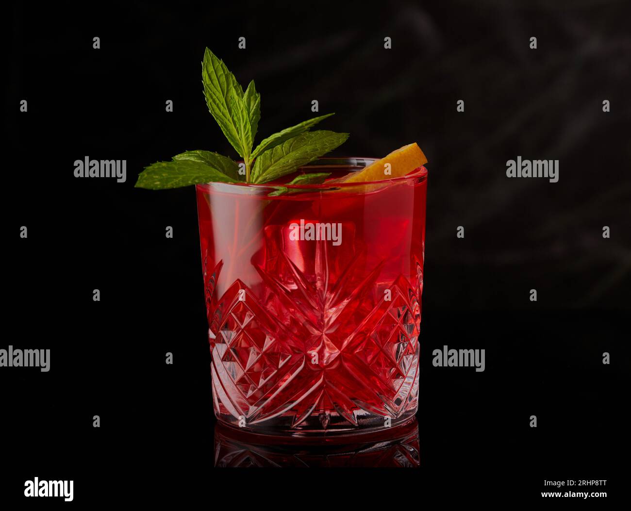 Red cocktail with ice and garnished with mint and a slice of lemon on a black background. Stock Photo