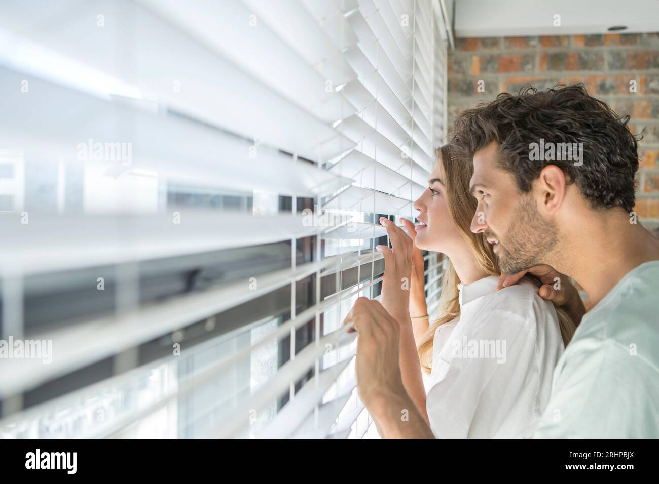 Couple looking through blind Stock Photo