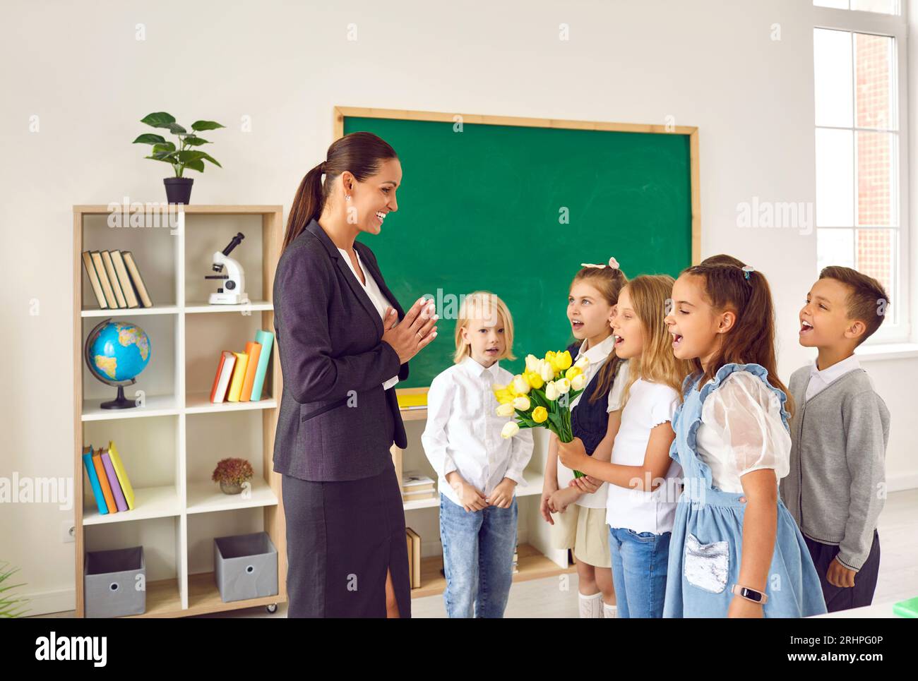 Children singing song congratulating happy teacher in school Stock