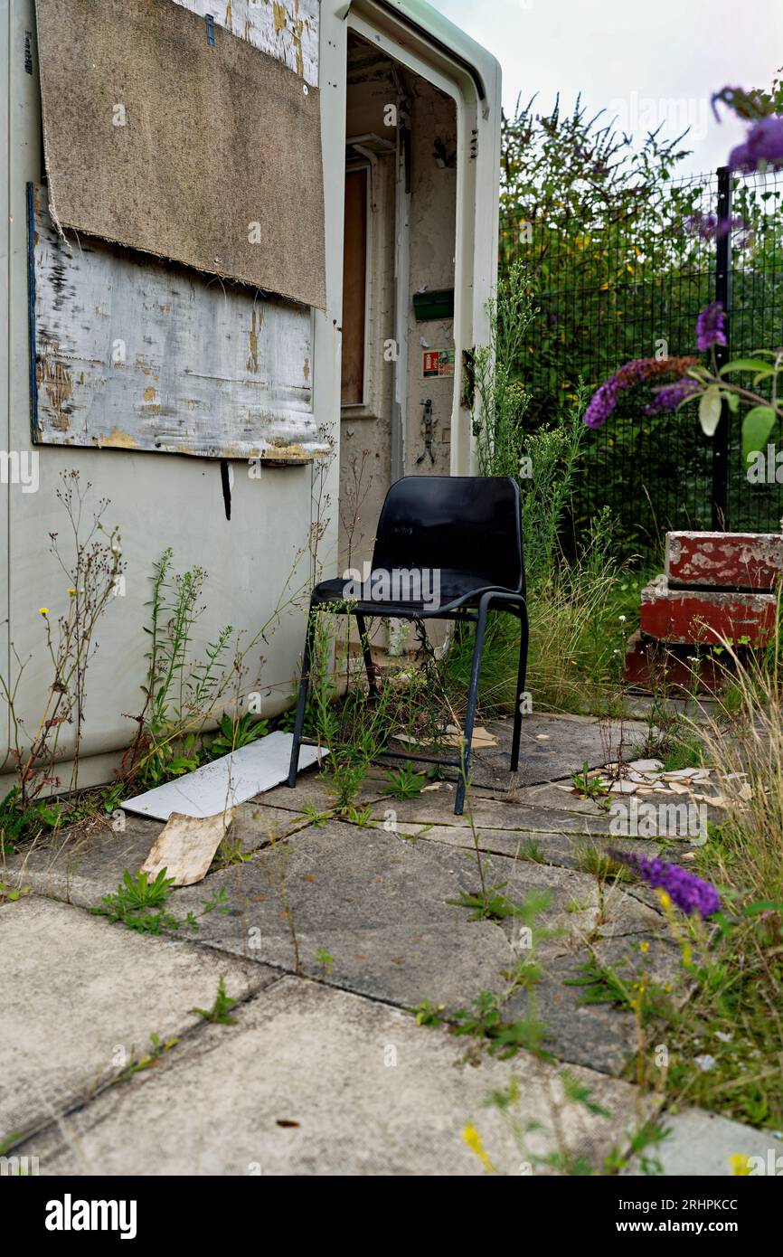 old black plastic office chair outside of decaying office building with over growing plants Stock Photo