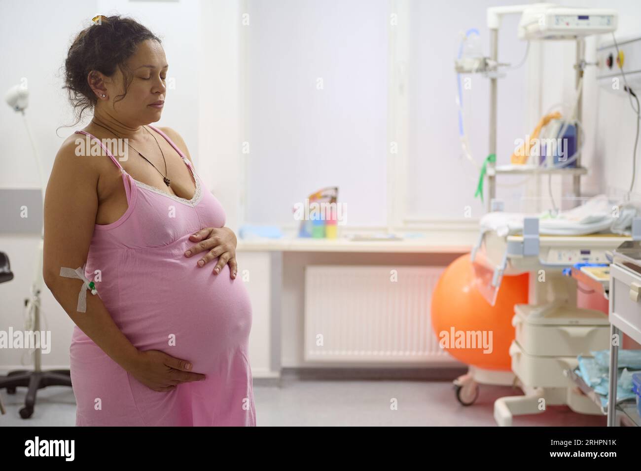 Multi-ethnic birthing mother having contraction, holding her big belly in the labor room of maternity hospital. Pregnancy. Easy delivery. Obstetrics a Stock Photo