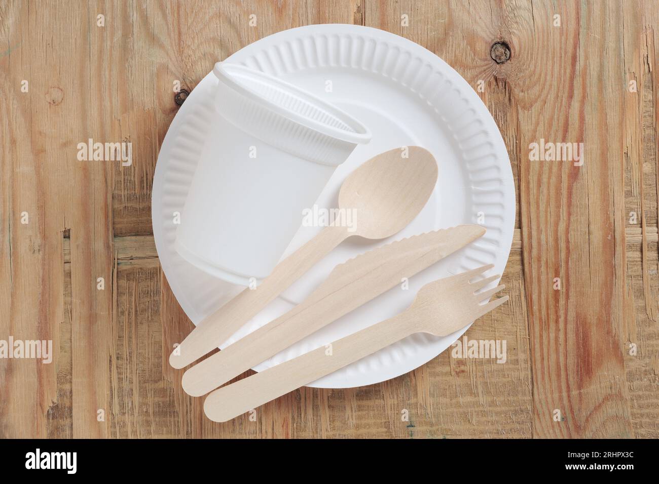 Paper plate, glass, wooden spoon, fork and knife on old wood, top view. Disposable tableware Stock Photo