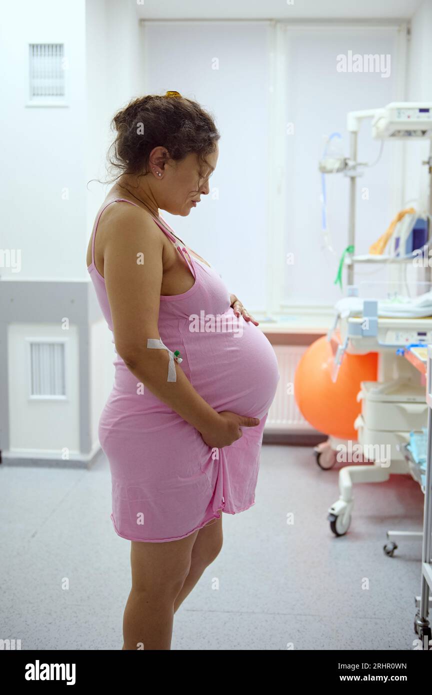 Side portrait of a pregnant woman, birthing mother holding her belly while having contraction during labor process, in hospital ward. Pregnancy. Easy Stock Photo