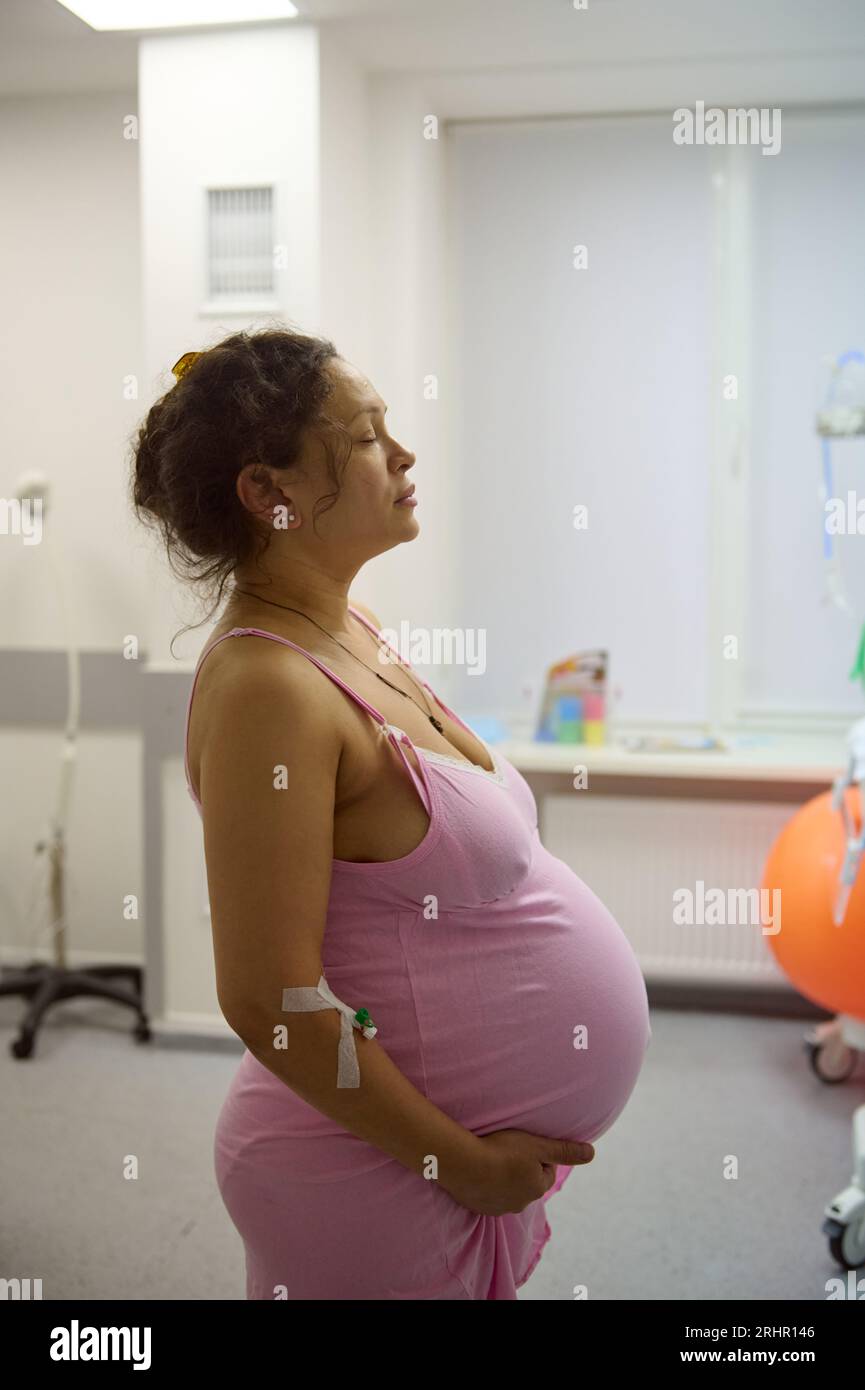 Pregnant woman, birthing mother in hospital ward, ready to delivery a baby, holding belly and practicing breathing exercises to induce an easy deliver Stock Photo
