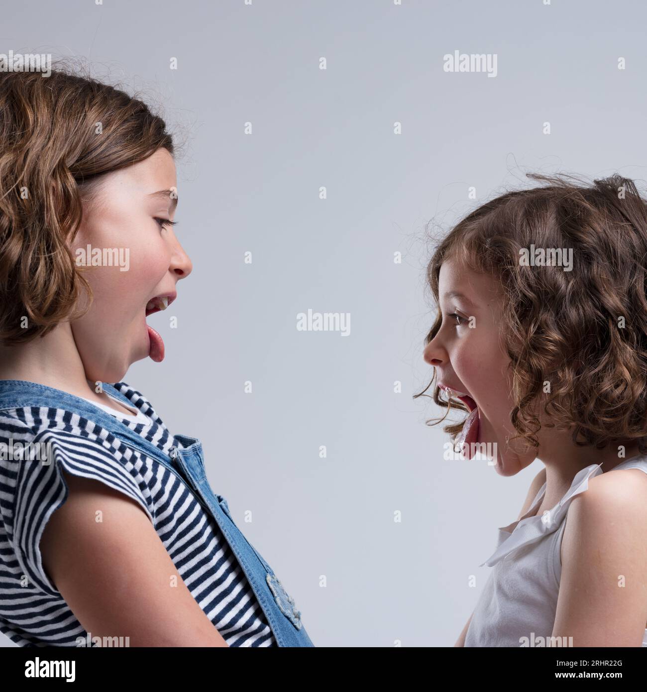 Young girls, possibly sisters or friends, teasing and making faces. Pictured side-by-side in casual attire, radiating happiness and laughter Stock Photo
