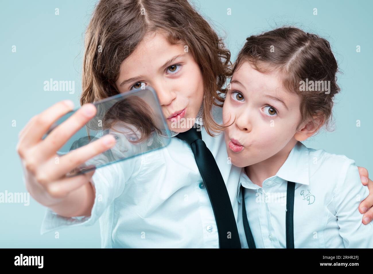 Two trendy girls take selfies, dressed in formal business attire, using advanced smartphones, emphasizing their image on social platforms Stock Photo