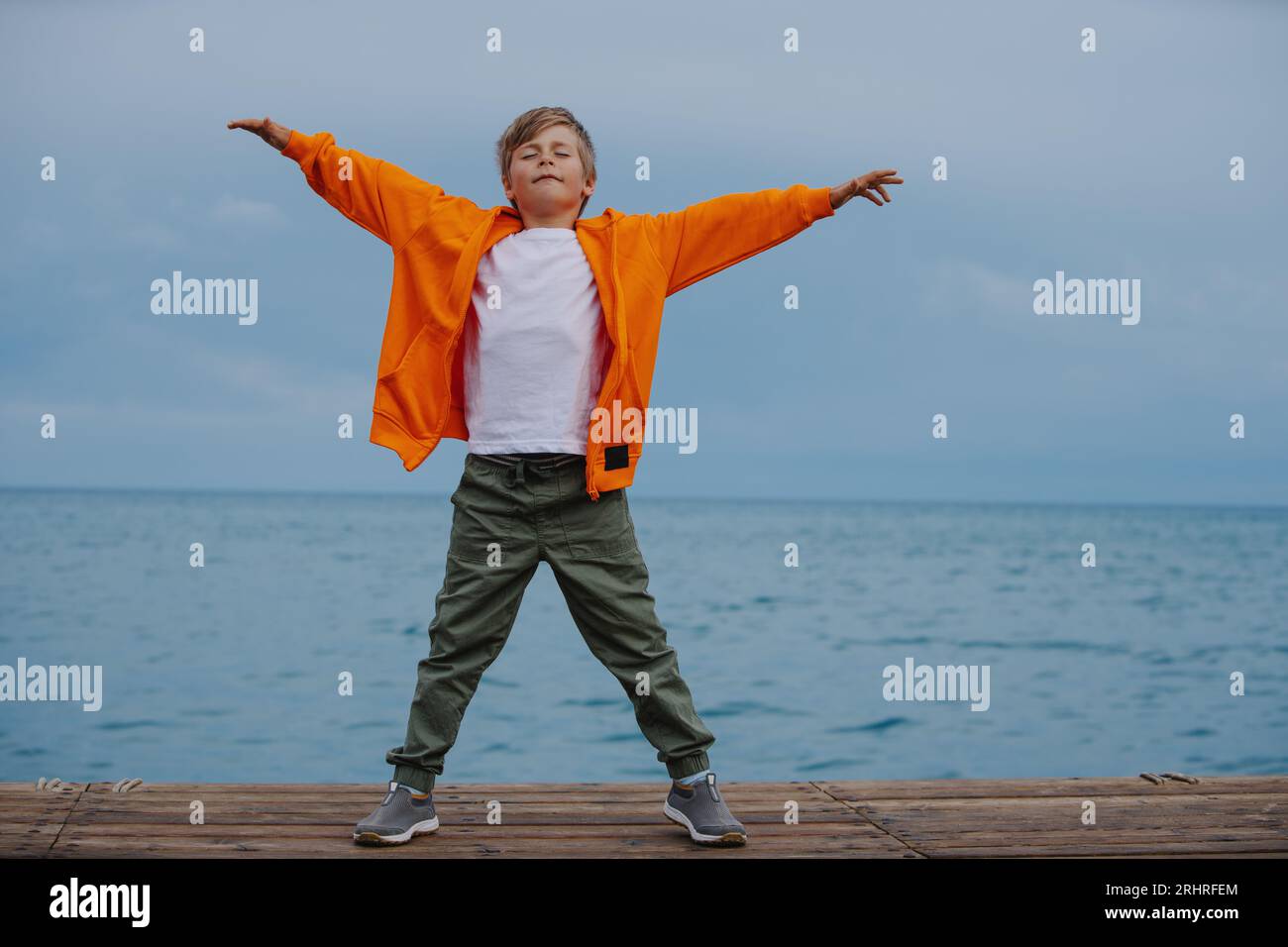 Happy boy standing on lake shore with his arms outstretched to the sides Stock Photo