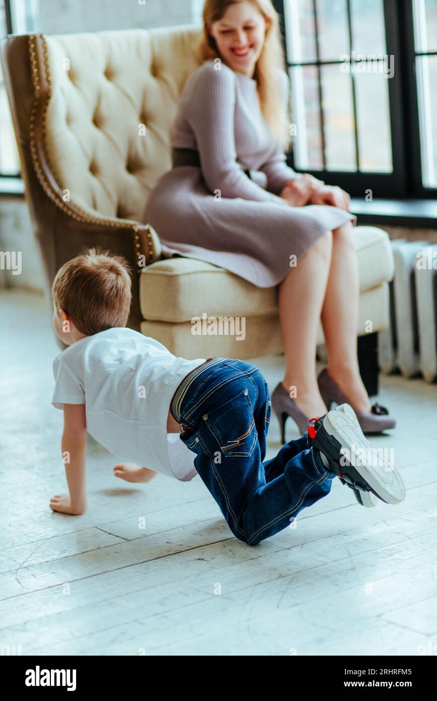Boy crawls on the floor next to his smiling mother in the room Stock Photo