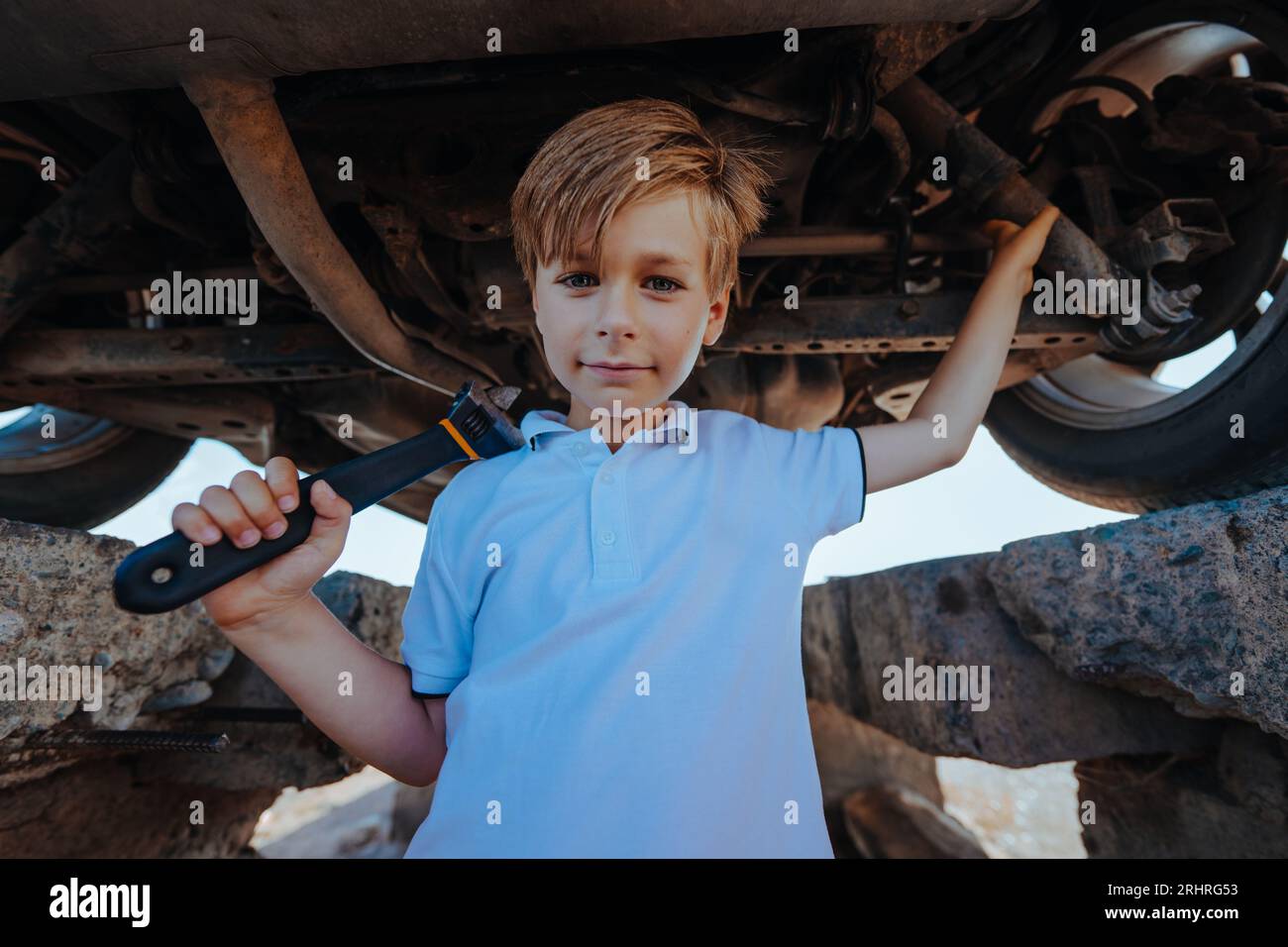 Cute boy automotive mechanic standing under car bottom with wrench Stock Photo
