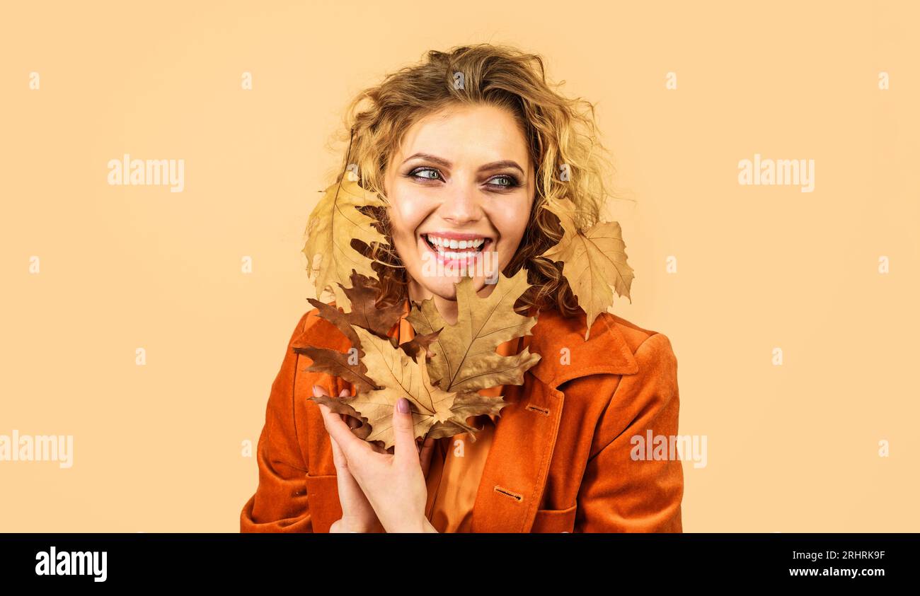 Happy beautiful girl with autumn leaves. Smiling autumn woman with yellow foliage. Stylish blonde model in orange shirt and coat with fall leafage Stock Photo
