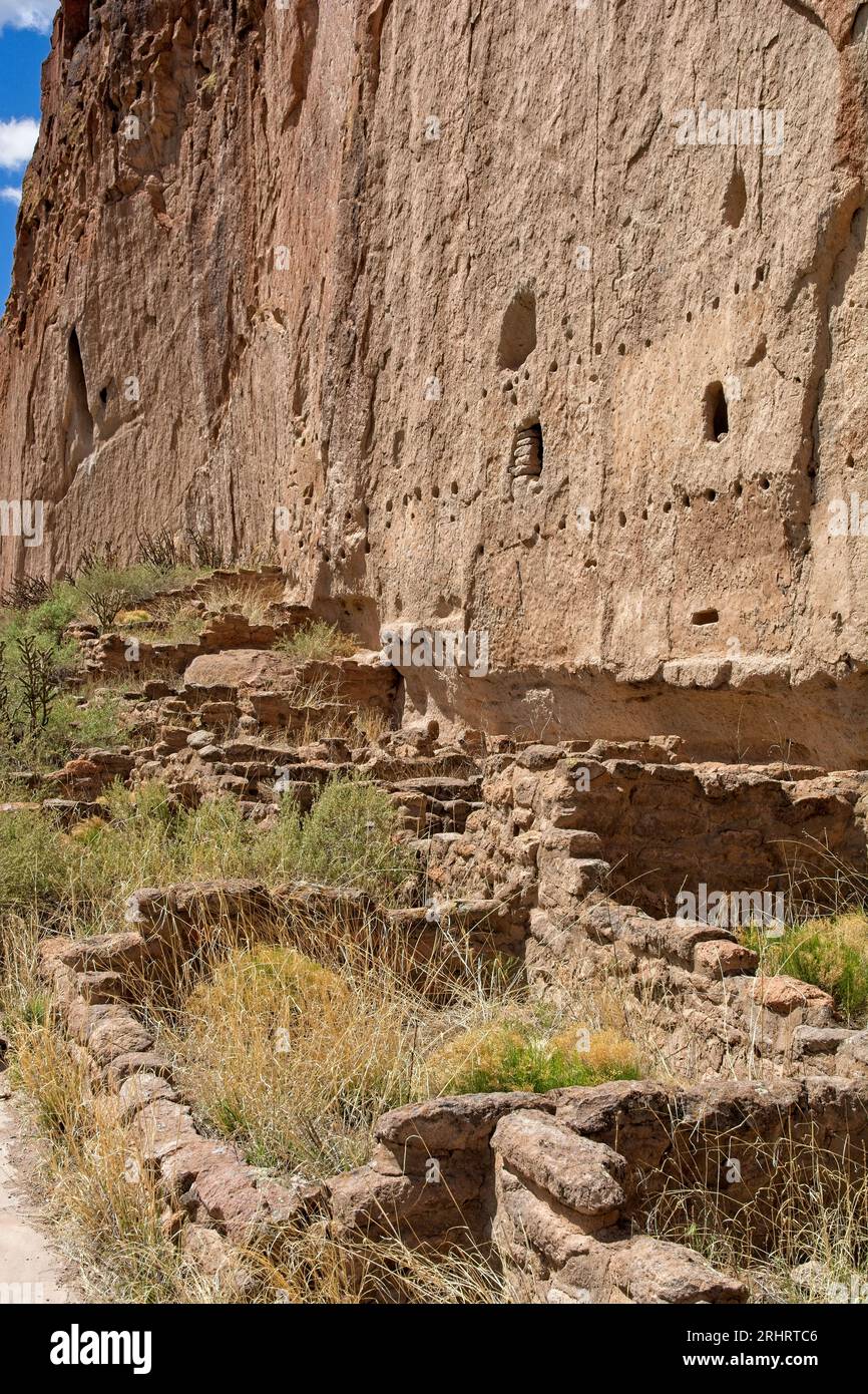 Ruins of stone foundations before petroglyphs carved into the volcanic ash tuff coated canyon walls by ancient Puebloan cliff dwellers Stock Photo