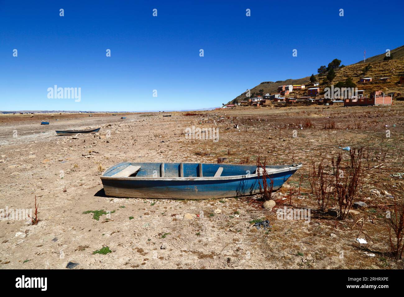 Lake Titicaca, BOLIVIA; August 18th 2023: Wooden rowing boats on the dried up shore of Cohana Bay on the Inner Lake / Huiñay Marka (the smaller part of Lake Titicaca) near the village of Cohana (in the background). Water levels in Lake Titicaca are approaching the record low level set in 1996, the lowest since Bolivia's weather service (Senhami) started keeping records in 1974. Many are blaming climate change; the last few years have been drier than normal and El Niño is currently strengthening in the Pacific Ocean off South America. Stock Photo