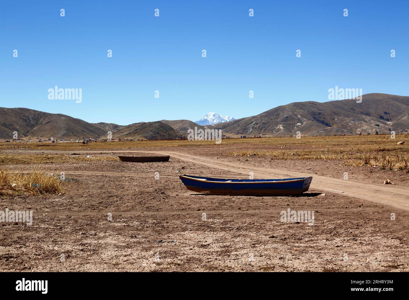 Lake Titicaca, BOLIVIA; August 18th 2023: Wooden rowing boats on the dried up shore of Cohana Bay on the Inner Lake / Huiñay Marka (the smaller part of Lake Titicaca) near the village of Cohana. In the background is Mt Huayna Potosi (6088m) in the Cordillera Real range of the Andes. Water levels in Lake Titicaca are approaching the record low level set in 1996, the lowest since Bolivia's weather service (Senhami) started keeping records in 1974. Many are blaming climate change; the last few years have been drier than normal and El Niño is currently strengthening in the Pacific Ocean off South Stock Photo