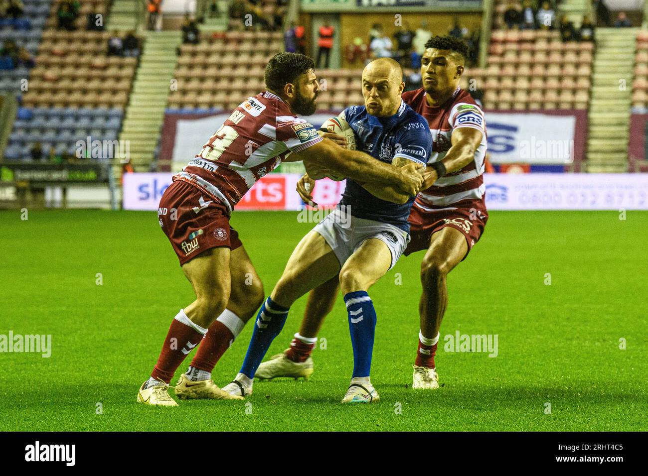 Hull FCs Adam Swift is tackled by Warriors Abbas Miski and Junior Nsemba during the BetFred Super League match between Wigan Warriors and Hull Football Club at the DW Stadium, Wigan on