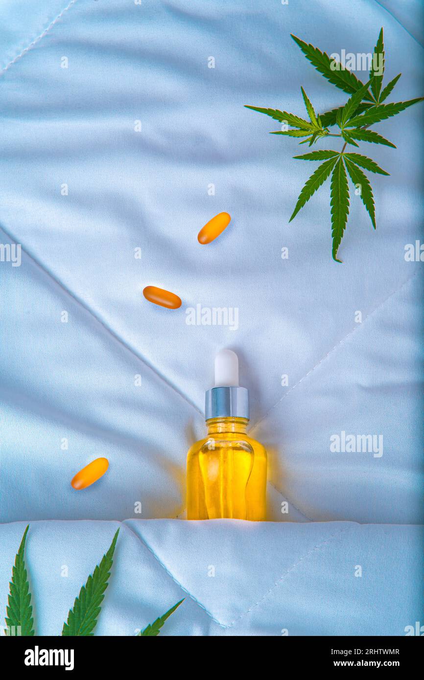 Bottle of cannabis oil, CBD, and a marijuana leaf, sleeping under the covers. Creative concept of cannabidiol products for better sleep and against in Stock Photo