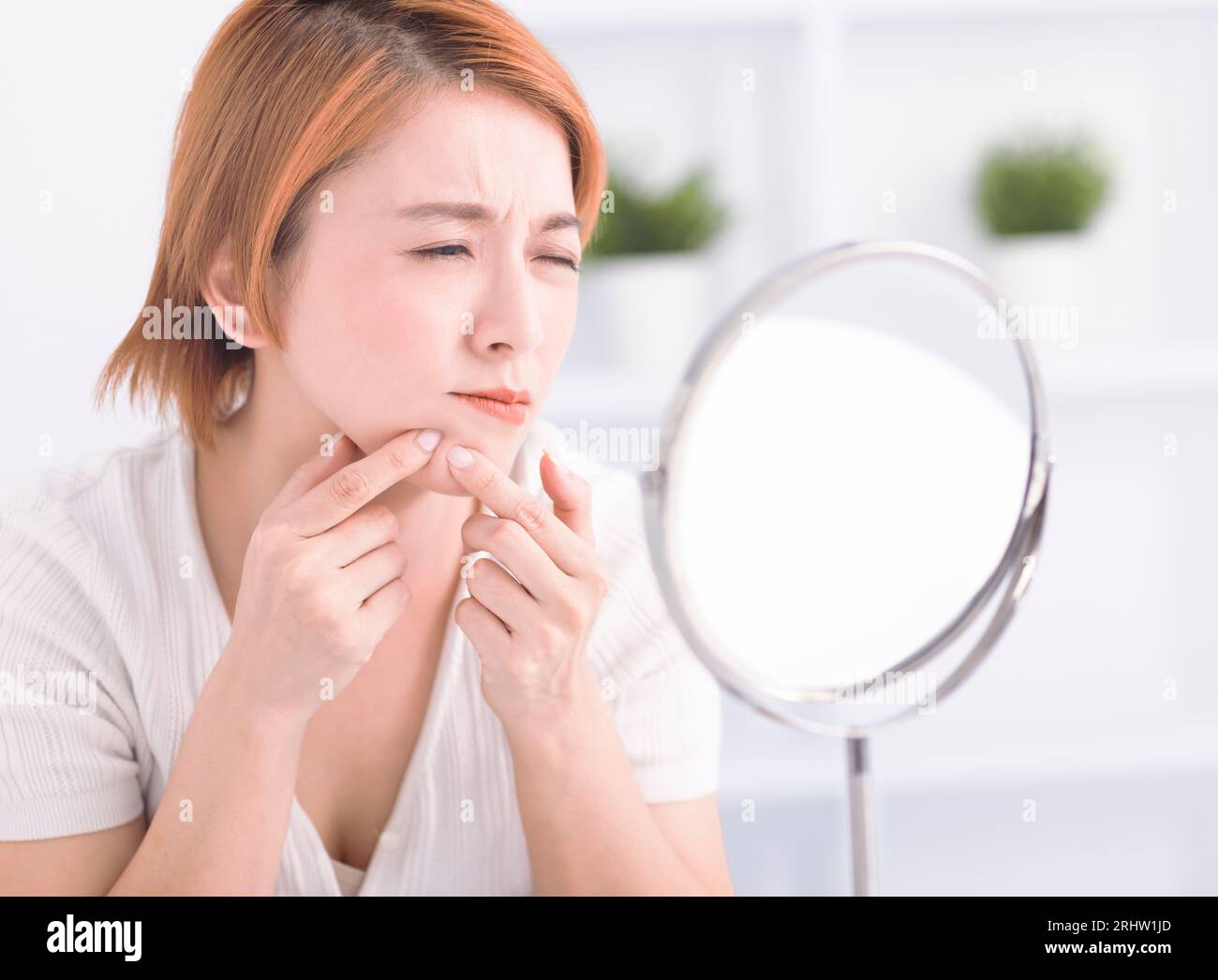 Young woman squeezing pimple spot for removing from face. Stock Photo