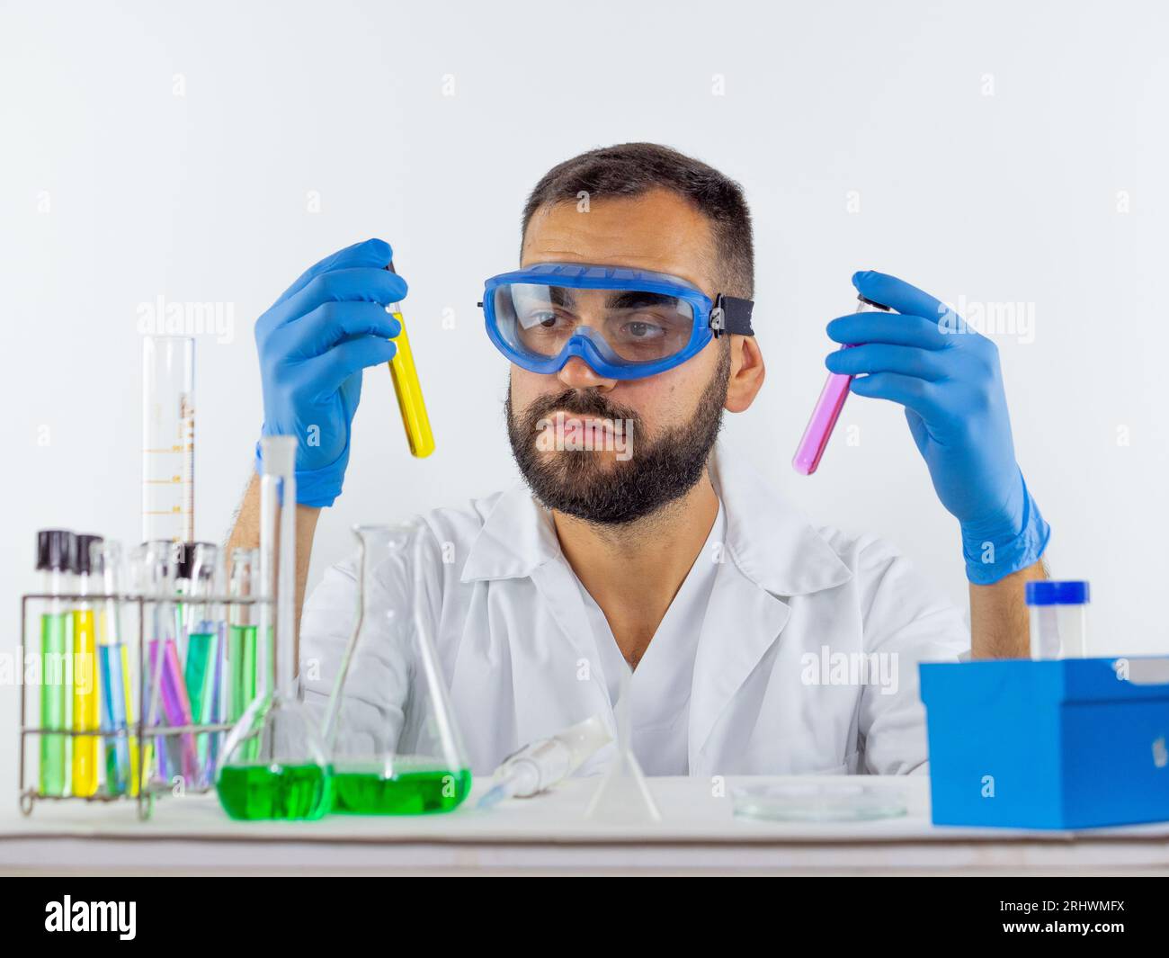 Young male scientist wearing protective glasses comparing two liquid samples in test tubes Stock Photo