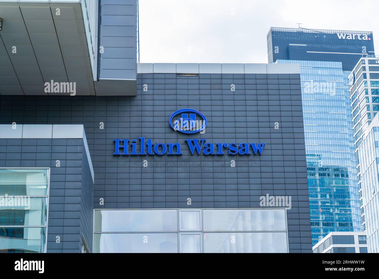 The building and logo of the Polish hotel Hilton Warsaw. Office building skyscraper in the city center. Entrance facade. Warsaw, Poland - July 26, 2023. Stock Photo