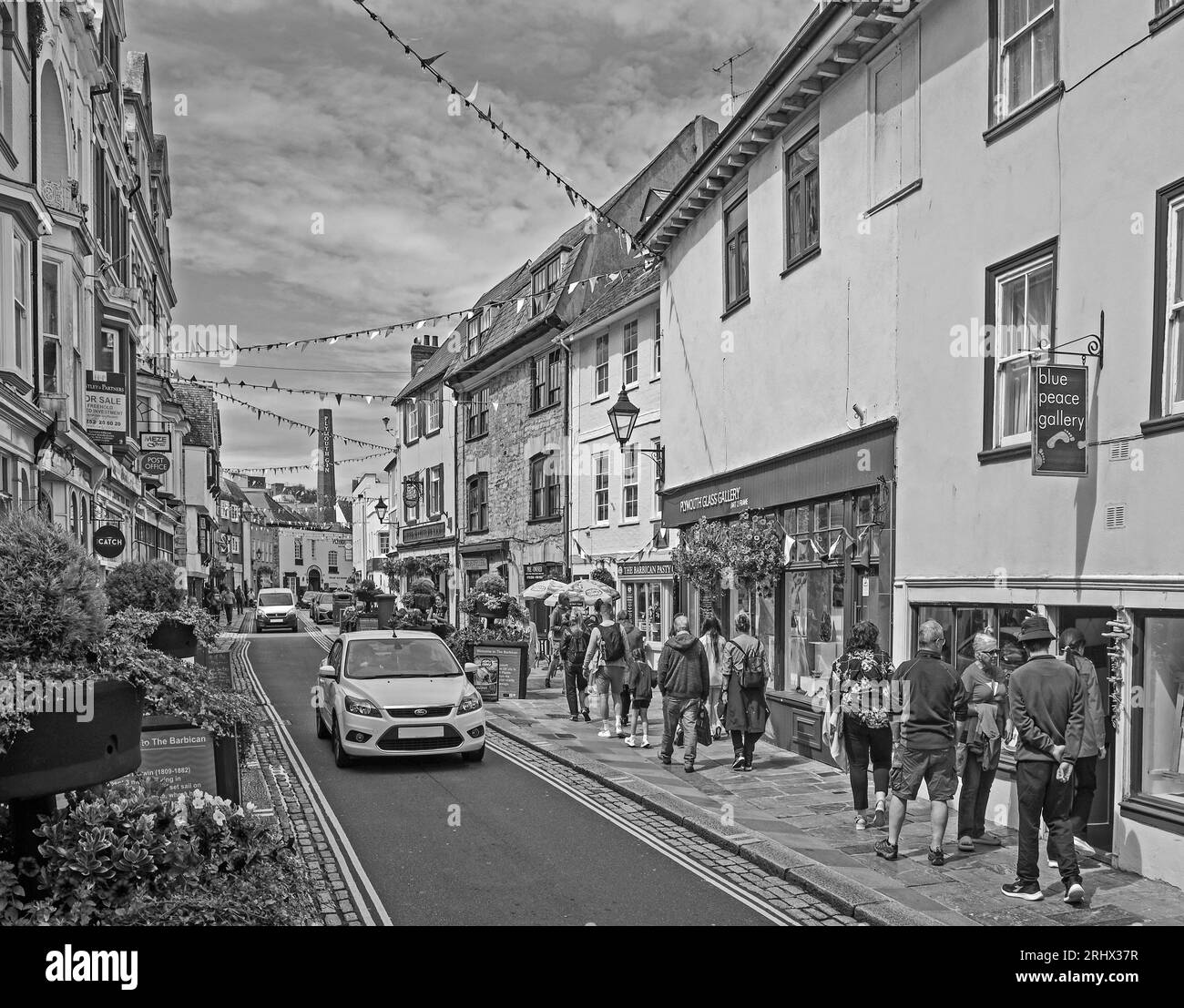 Monochrome image of Flower tubs and bunting bring a celebratory feel to Southside Street on Plymouth’s historic Barbican. A quirky mix of small shops, Stock Photo