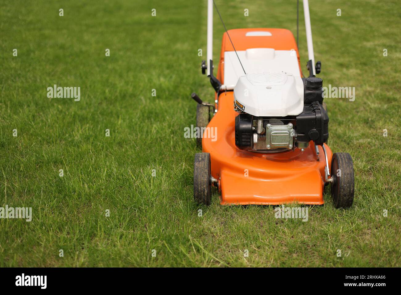 Top view of modern orangegrey electric lawn mower cutting bright lush