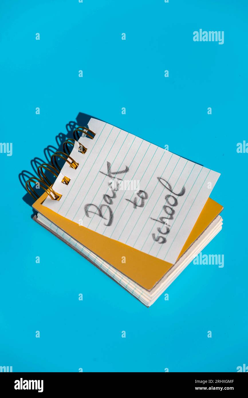 From above of opened spiral notebook with hardcovers and parallel lines page with message back to school written placed against blue wall Stock Photo