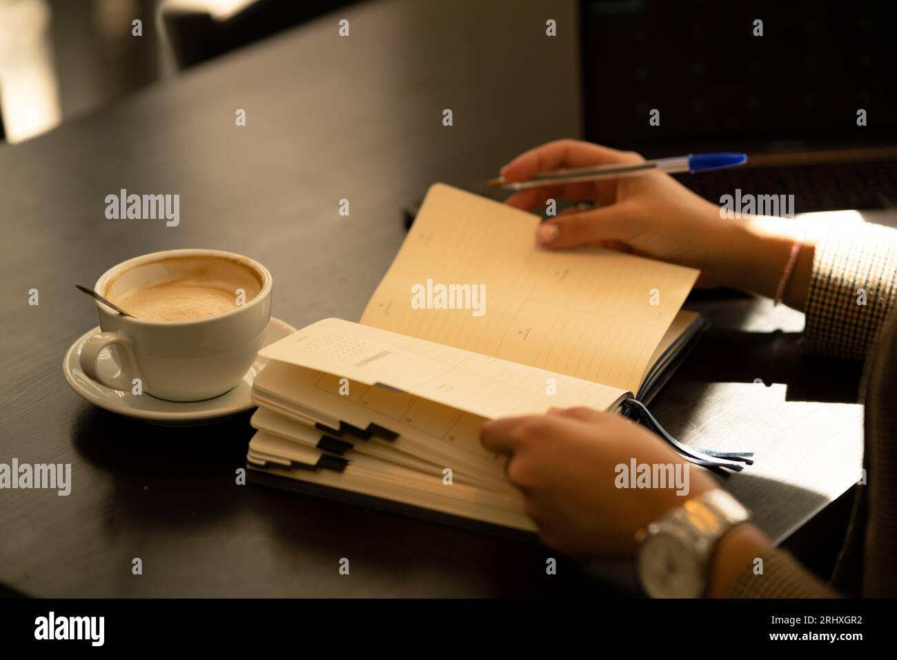 Anonymous young while sitting at table with notebook and taking notes with pen in cozy blurred cafe Stock Photo