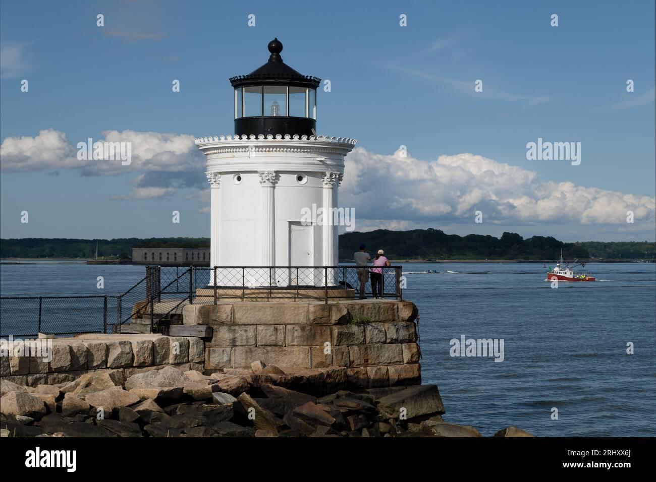 A lobster boat is coming into the harbor by Portland Breakwater Lighthouse, also known as 'Bug Light.' It is a favorite Maine tourist attraction. Stock Photo