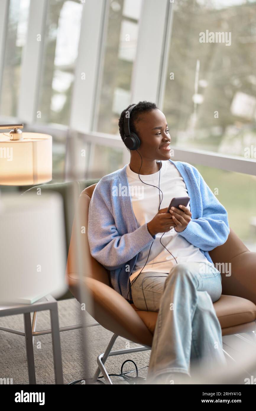 Happy African Black gen z girl wearing headphones using phone, vertical ...